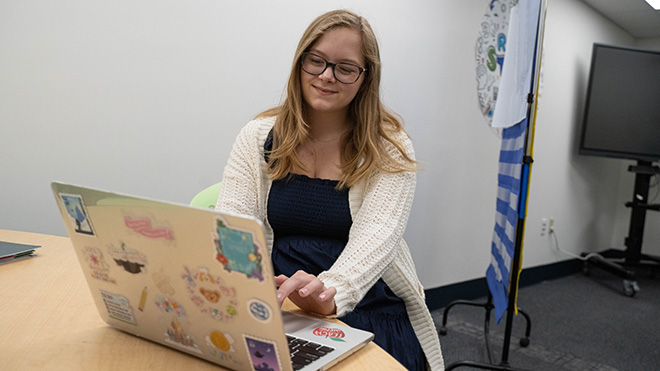 Senior Marisa Cestone sits at a desk and looks at her laptop, which is covered in stickers
