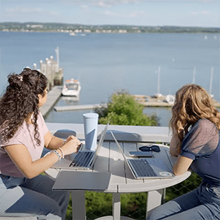 Two students sit at a table outside the sailing center looking out at the bay