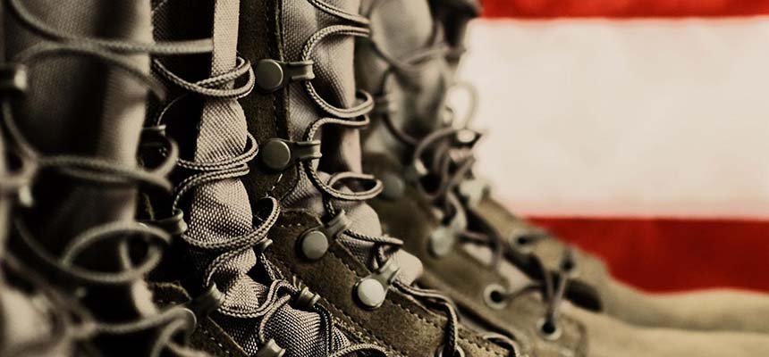 A close up photo of army boots with an American flag in the background.